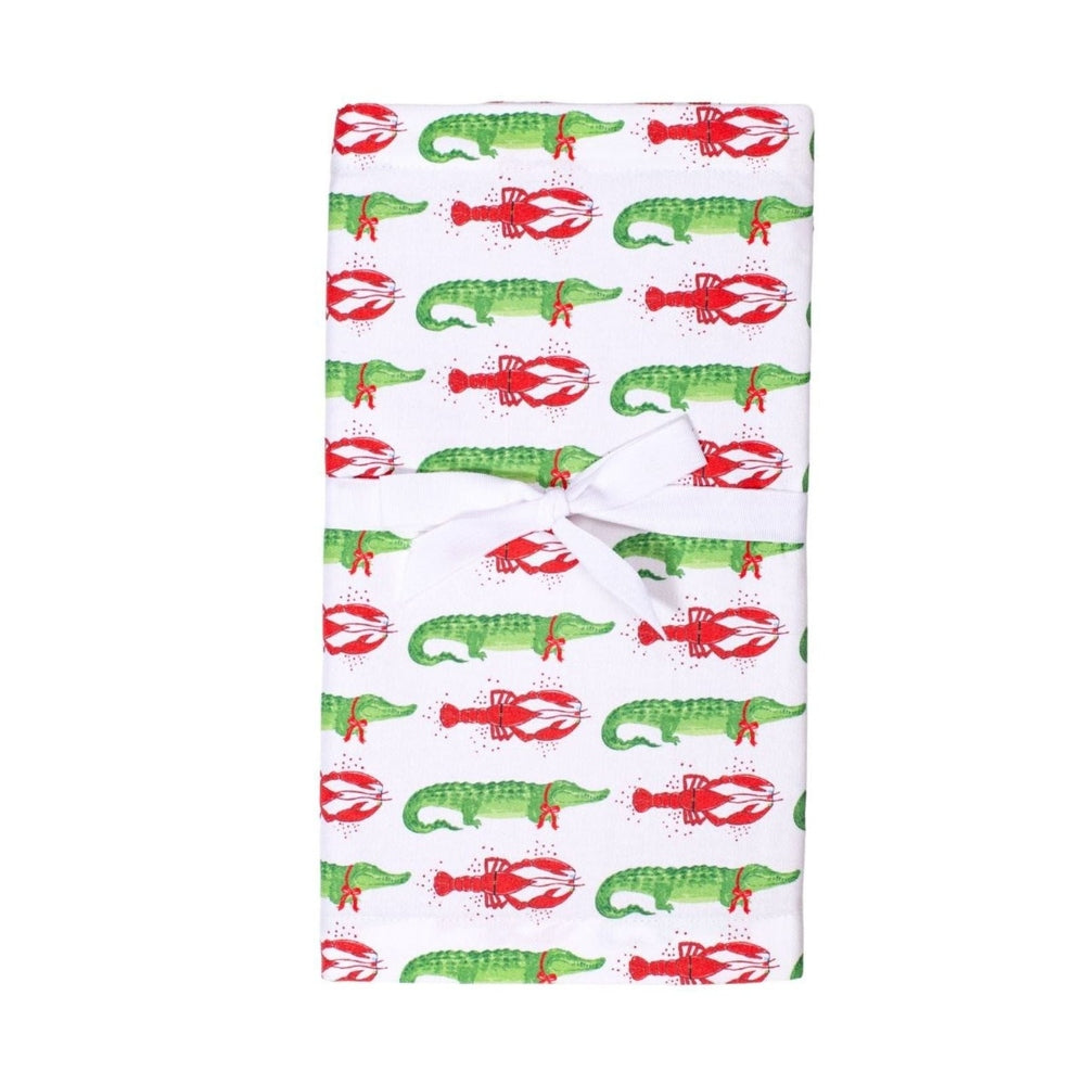 White tea towel with repeating pattern of green alligators and red lobsters tied with a white ribbon