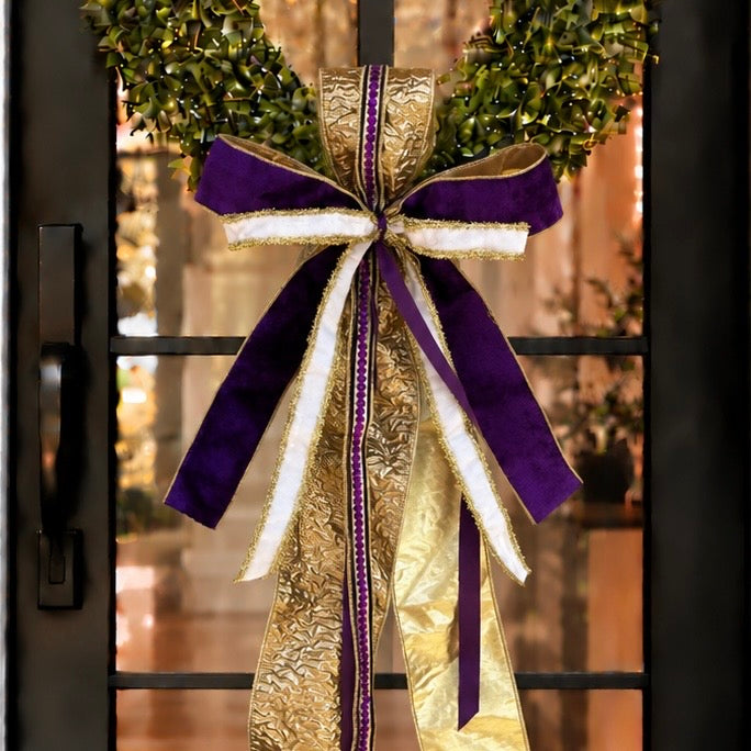 Door sash and bow in purple velvet, white and gold ribbon on a boxwood wreath