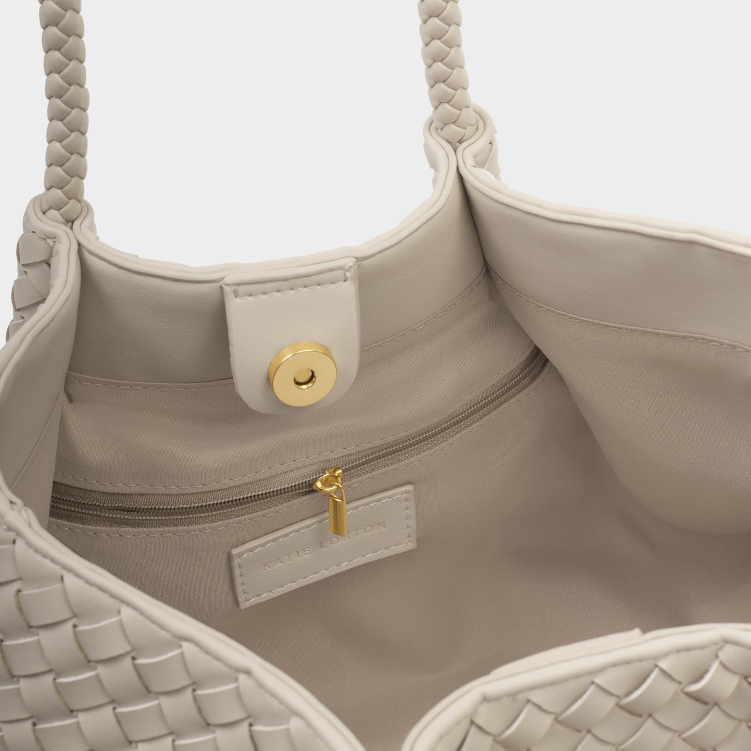Vegan leather handbag by Katie Loxton showcasing the interior compartment of an off-white woven tote featuring a gold magnetic closure, branded logo label, and intricate braided straps