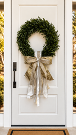 White front door with a boxwood wreath and a gold and silver-white ribbon bow
