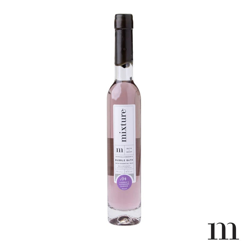 Product photograph by Mixture of a slender glass bottle of Lauren's Lavender Garden bubble bath featuring pale purple liquid, a black wax-dipped cap, and a minimalist white label with a purple circular emblem against a white backdrop