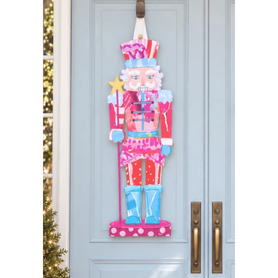 Painted nutcracker door hanger in pink, red and blue holding a gold star wand on a light blue door