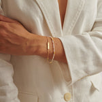 Person wearing a gold chain bracelet with a rectangular charm and a beaded bracelet with gold accents