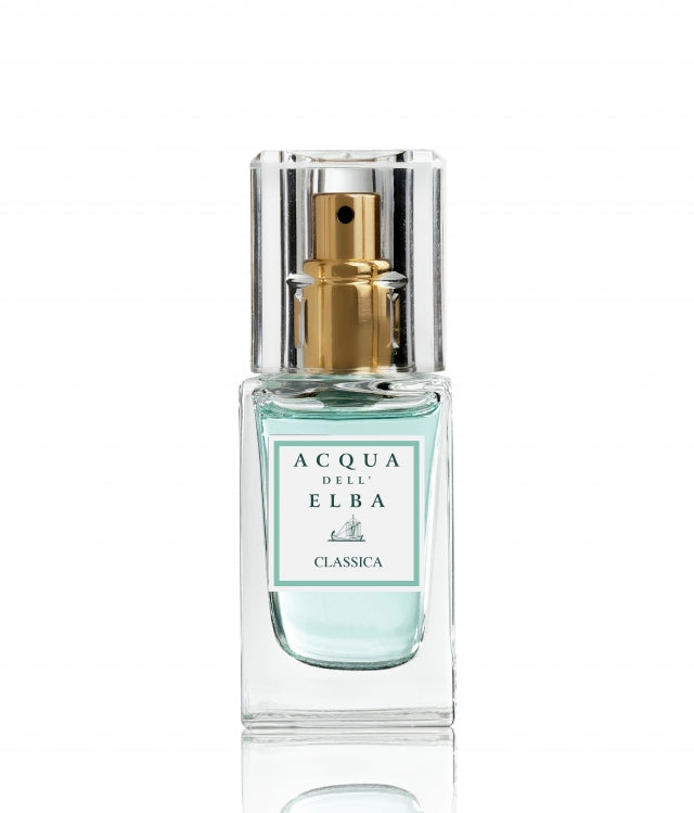 A bottle of Classica Donna perfume by Acqua di Elba, surrounded by floral arrangements and citrus fruit.