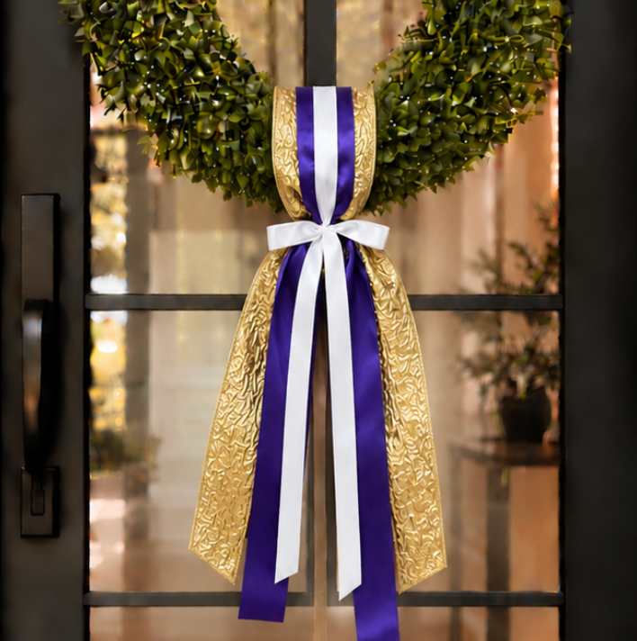 Green boxwood wreath with purple white and gold ribbon hanging on a glass door