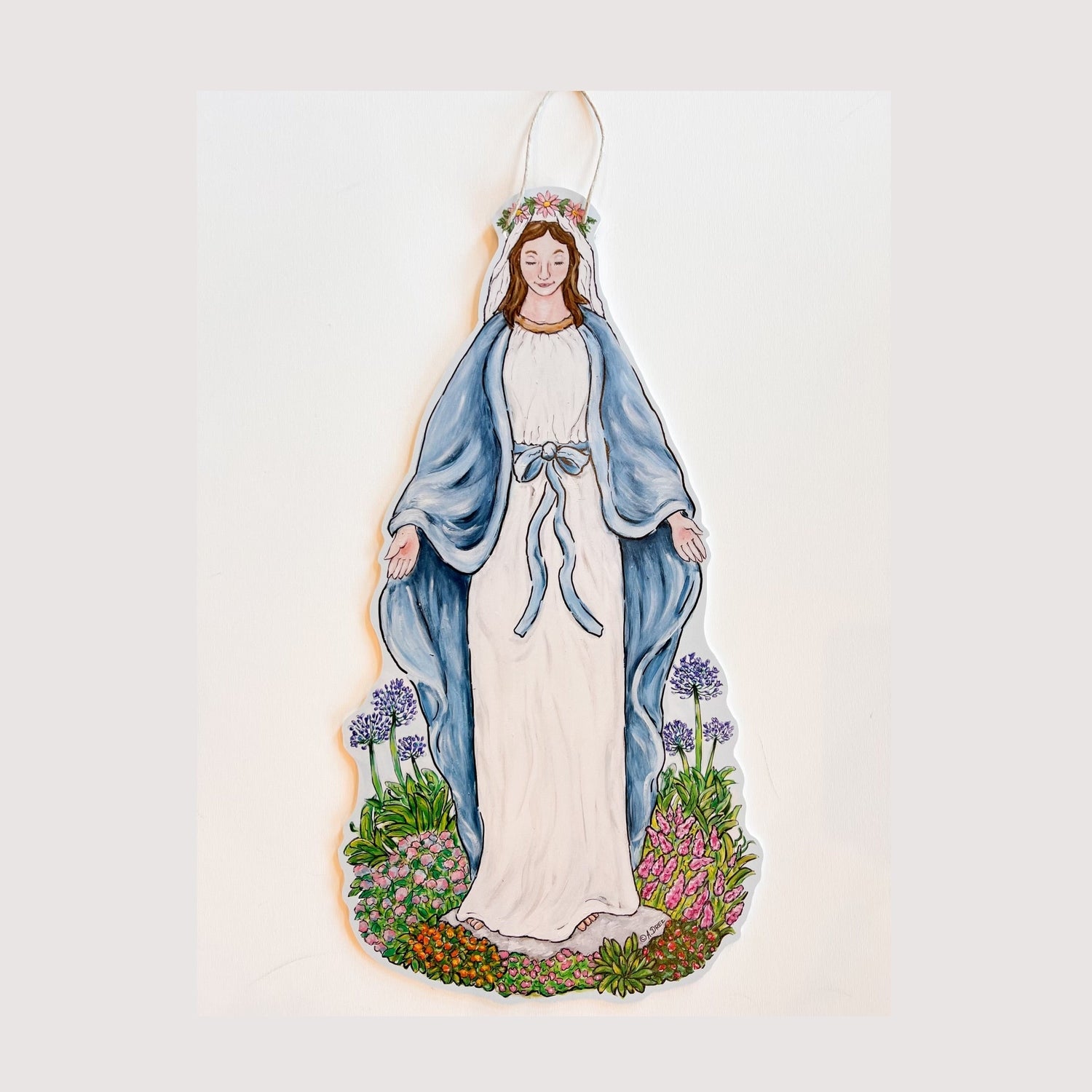 A door hanger featuring an illustration of a woman in a white and blue robe, with a halo, standing in a garden.