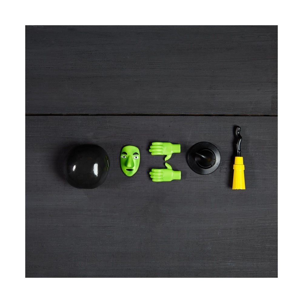 Witch costume accessories including a green face mask hands hat and broom on a black wooden surface