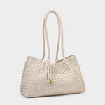 Woven leather tote bag by Bottega Veneta showcased in a studio setting featuring a cream-colored intrecciato pattern, long braided shoulder straps, and gold-toned square charms on decorative tassels