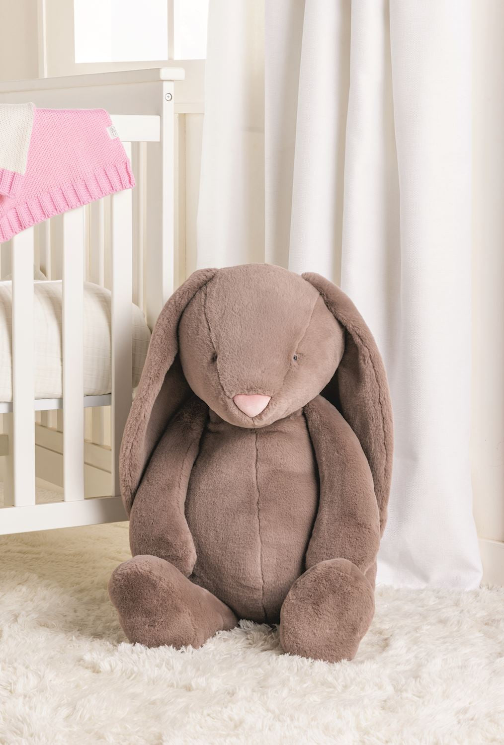 Brown plush bunny toy in a crib with white curtains and pink blanket