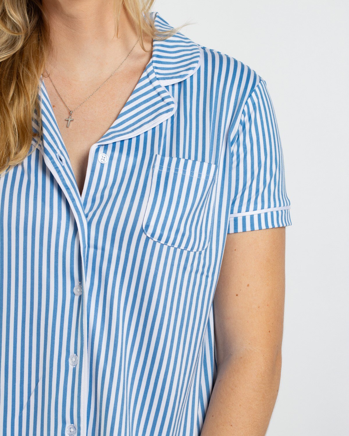 Person wearing a blue and white vertical striped short sleeve button down pajama top with a chest pocket