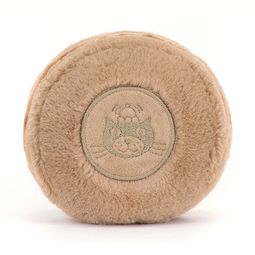 Back of a tan plush macaron with an embroidered round emblem of a cat in a chef's hat