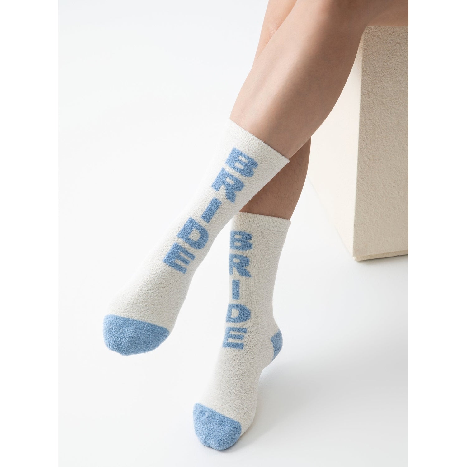 Cream fuzzy socks with blue Bride text and blue toe and heel accents worn on legs