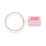 Beaded hair tie with turquoise beads and gold chain on a pink 'Beaded Blondes' packaging.