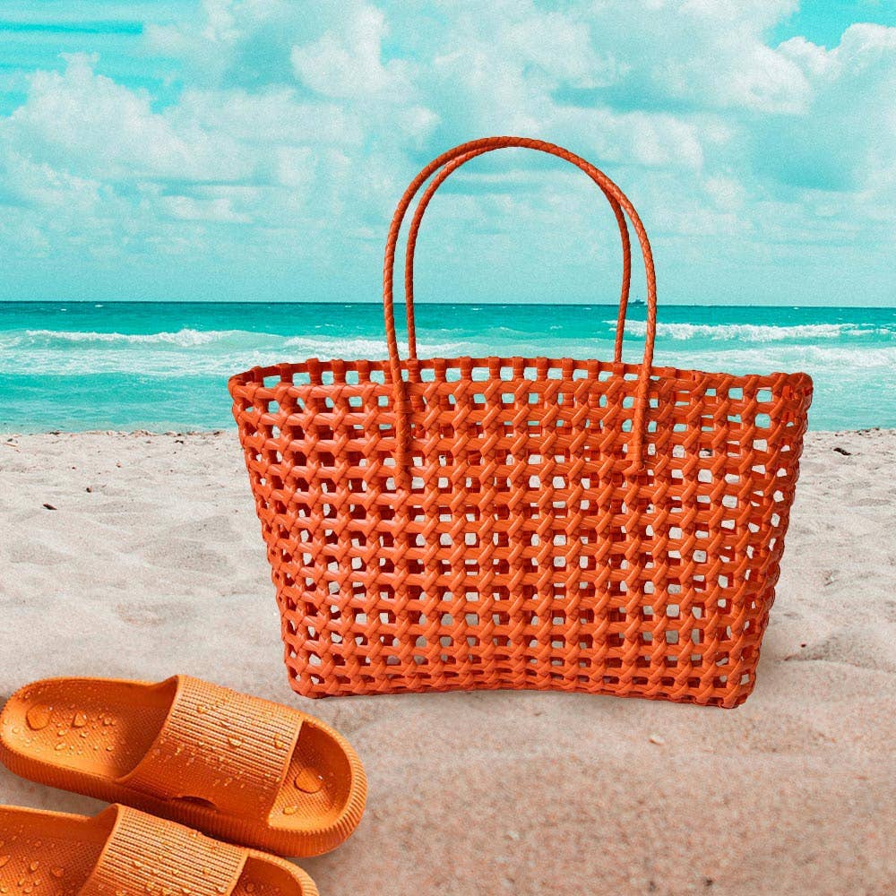 Orange woven bag and sandals on a sandy beach with ocean and sky in the background