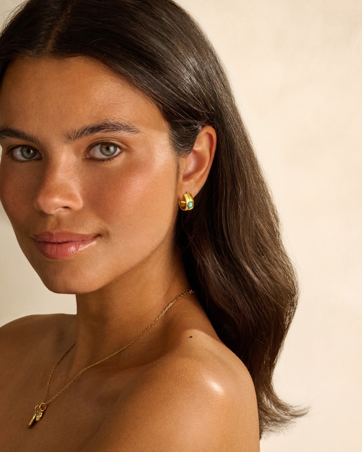 Woman wearing gold hoop earrings with turquoise stone and a gold chain necklace