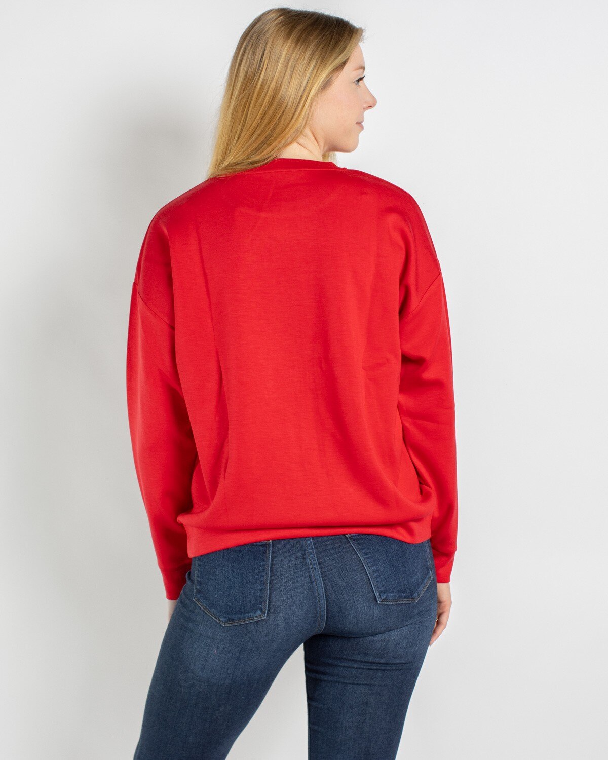 Woman seen from behind wearing a plain red long sleeve sweatshirt and blue jeans