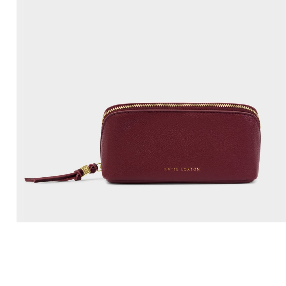 Vegan leather accessory by Katie Loxton featuring a burgundy travel pouch on a neutral backdrop with a gold-embossed brand logo, pebbled texture, and matching tassel zipper pull