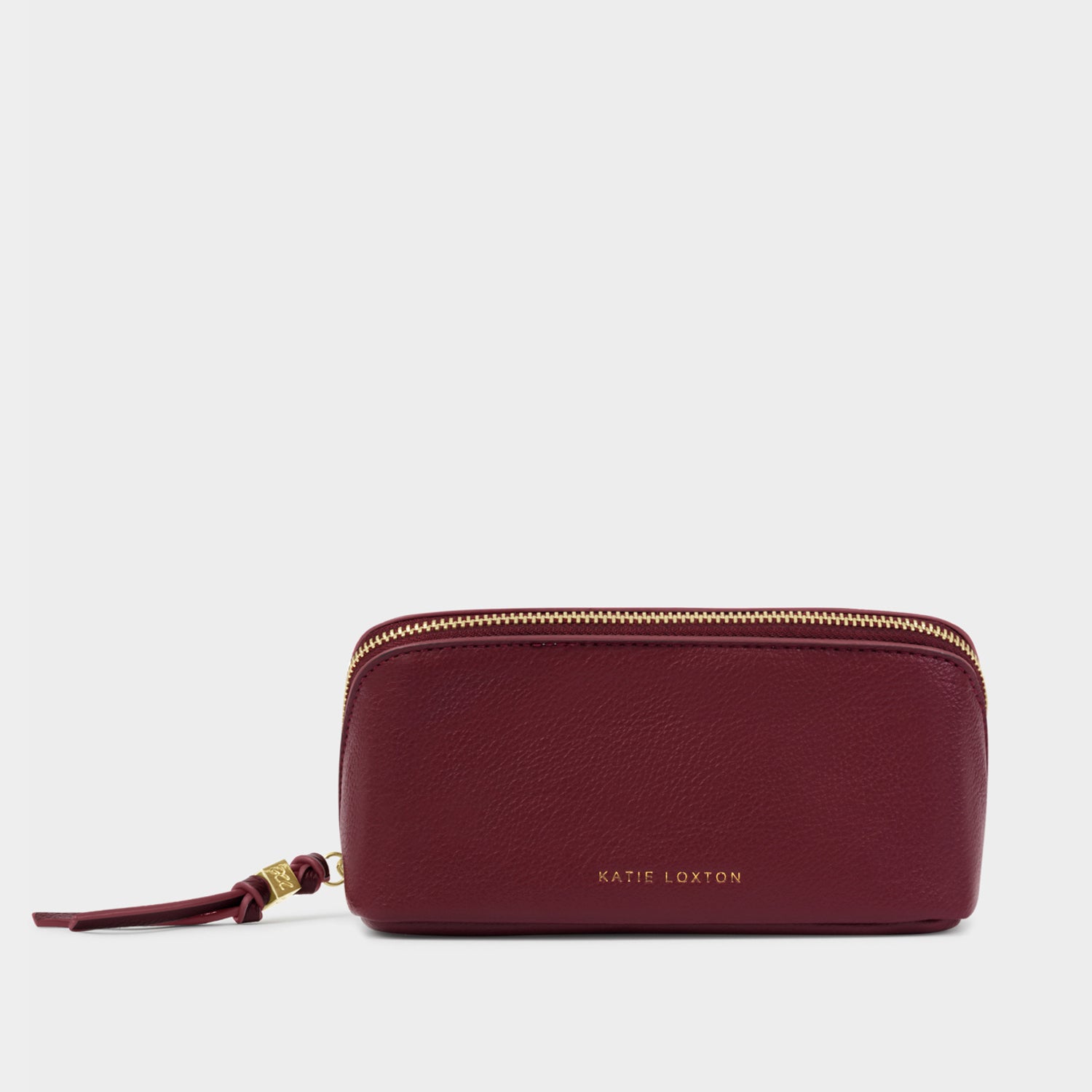 Vegan leather accessory by Katie Loxton featuring a burgundy travel pouch on a neutral backdrop with a gold-embossed brand logo, pebbled texture, and matching tassel zipper pull