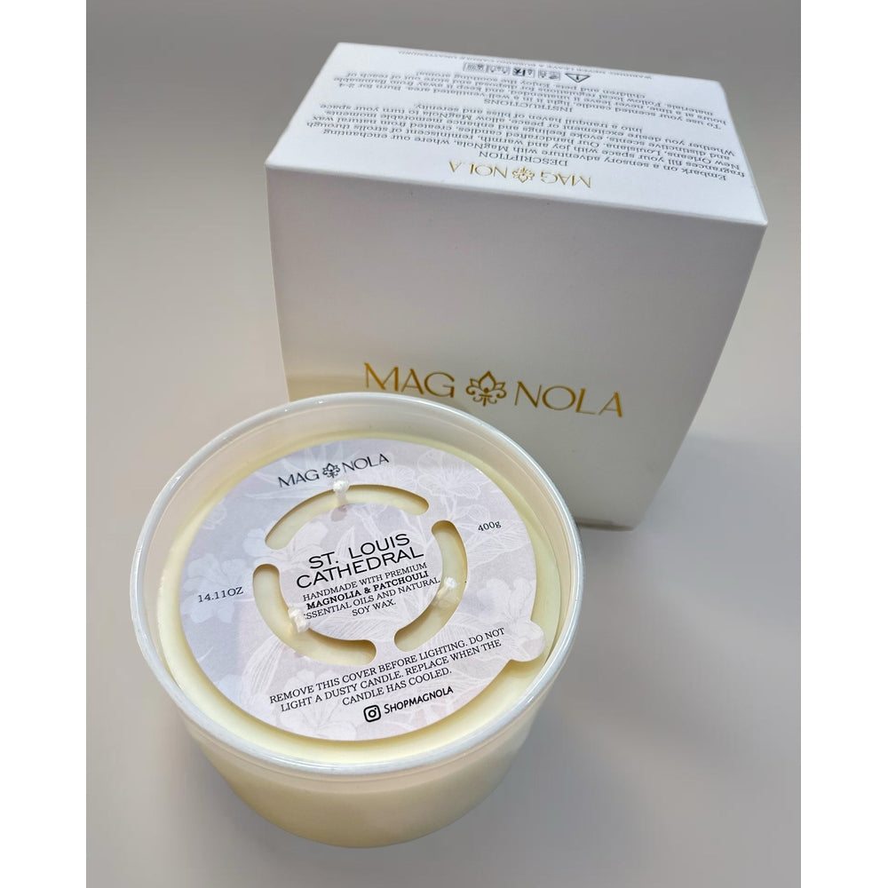 Magnola brand product photography of a St. Louis Cathedral scented candle in New Orleans featuring a gold foil logo, minimalist white box, and a decorative floral-patterned dust cover