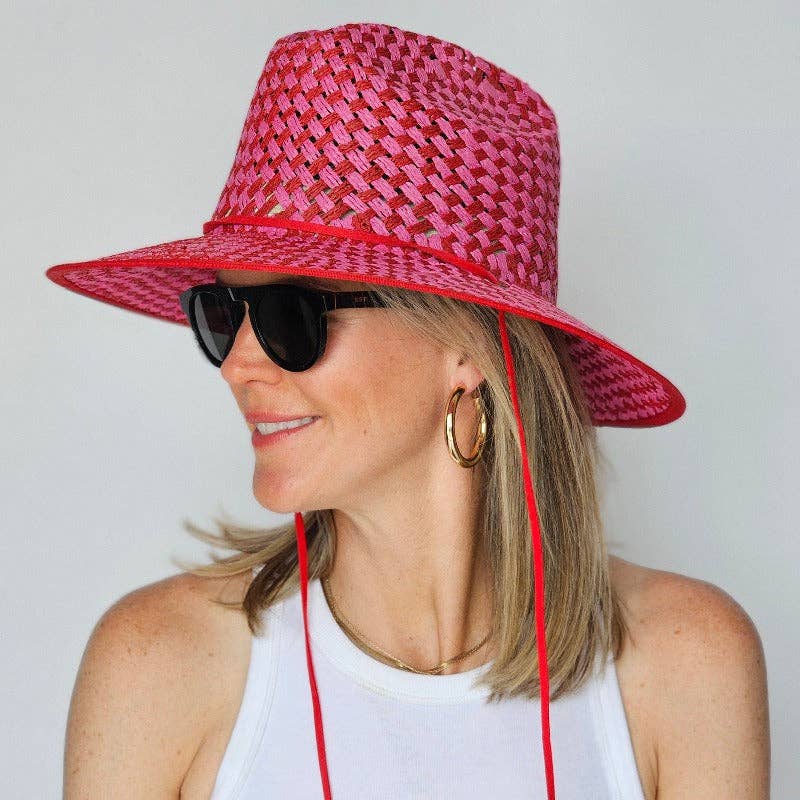 Person wearing a pink woven sun hat with a red strap on a plain background
