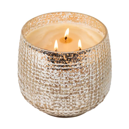 A gold-colored candle with a textured glass vessel and three wicks, burning with a warm glow.