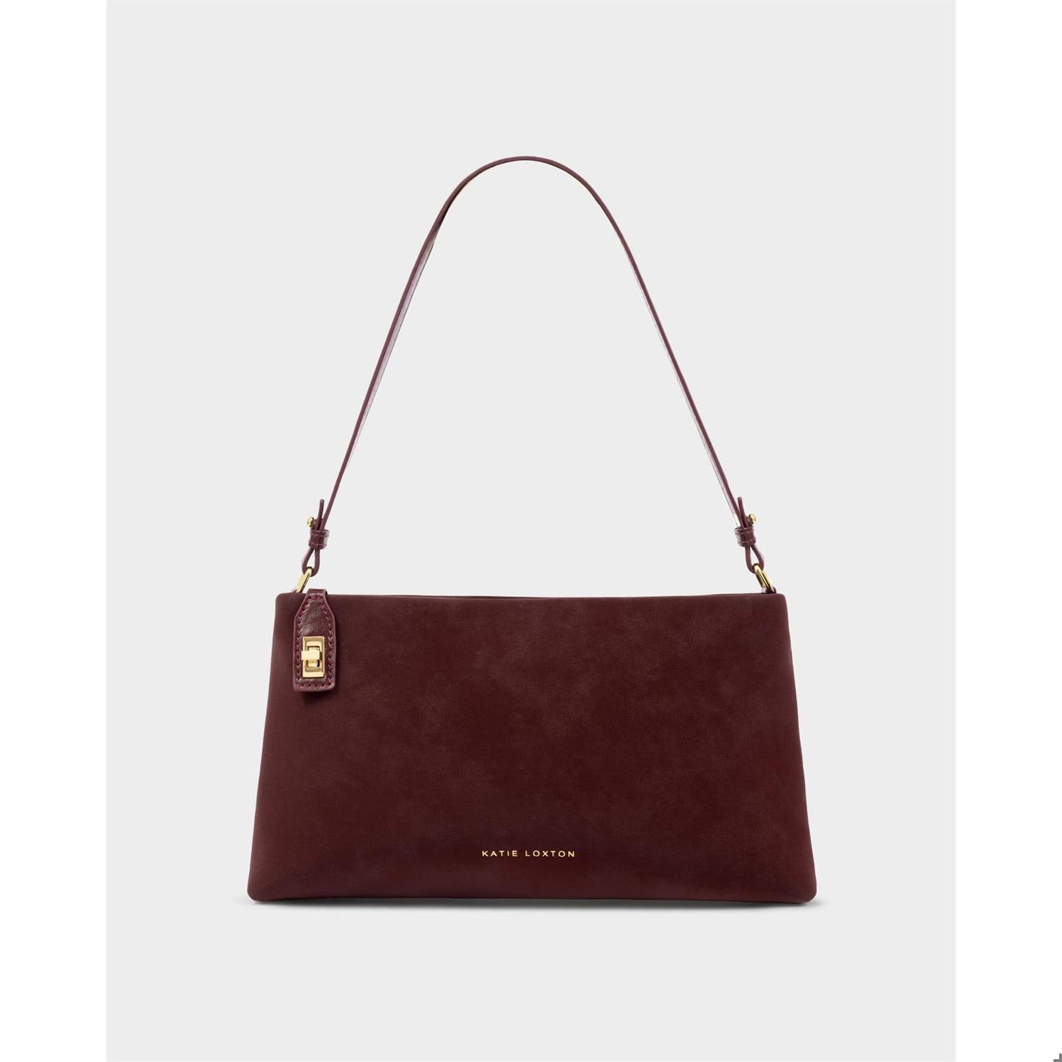 Product photograph by Katie Loxton of a deep burgundy faux suede shoulder bag in a studio setting featuring a gold-tone turn-lock tag, thin adjustable strap, and minimalist brand lettering