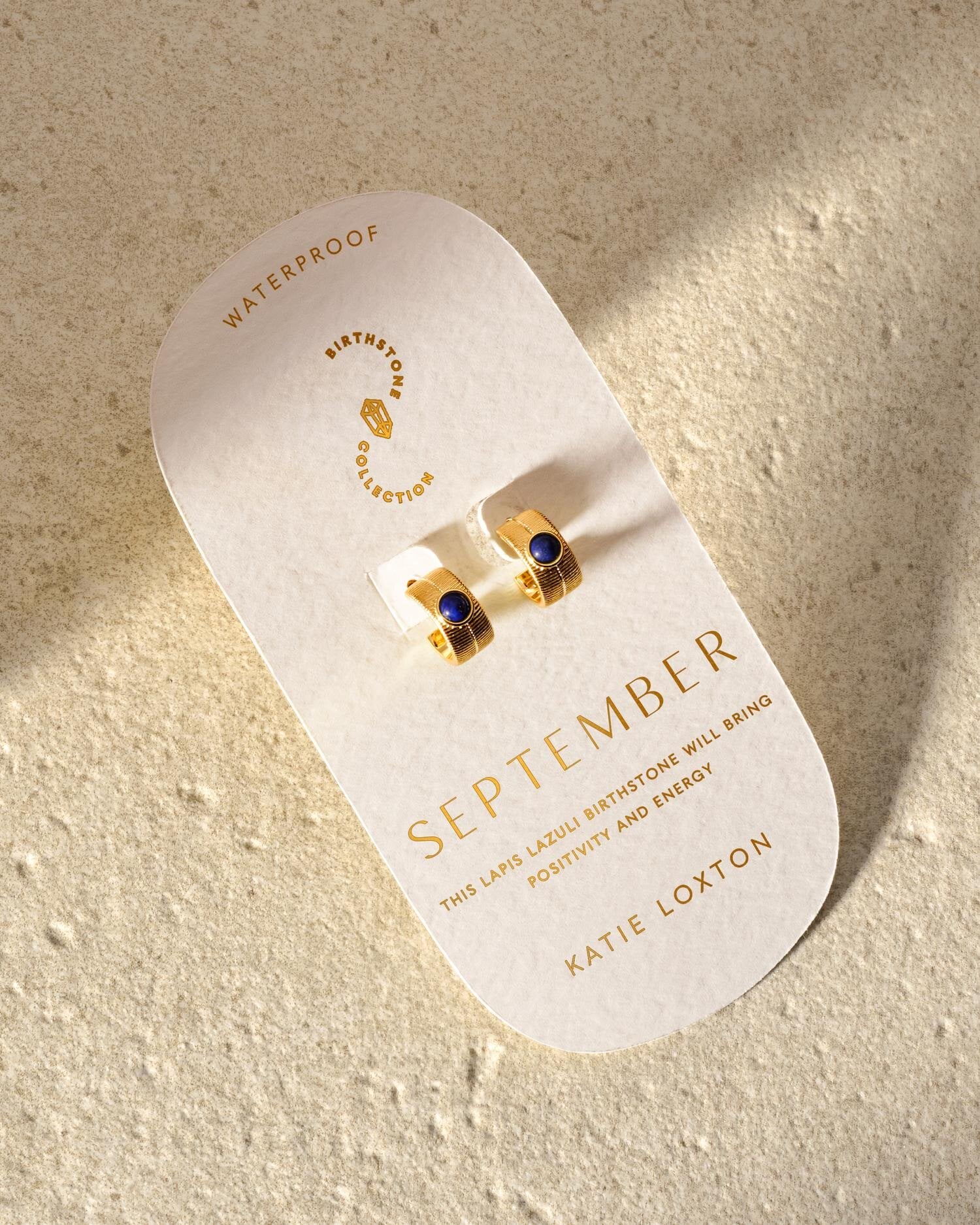 Gold hoop earrings with blue lapis lazuli stones on a September birthstone display card
