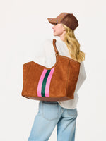 Woman wearing a brown suede tote bag with pink and green stripes over her shoulder