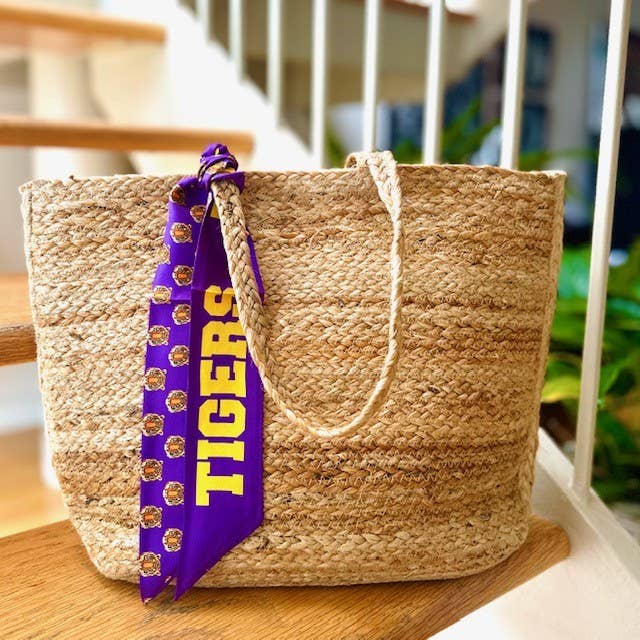 Purple twilly scarf with "TIGERS" in gold letters and tiger faces tied to the handle of a woven jute tote