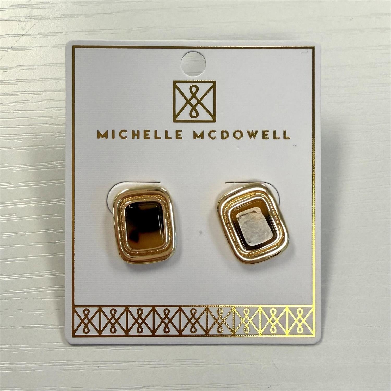 Jewelry by Michelle McDowell featuring a pair of rectangular stud earrings displayed on a white card with gold branding, highlighting polished gold frames and mottled brown tortoiseshell resin centers