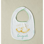 Baby bib with text and beignet illustration on a beige background