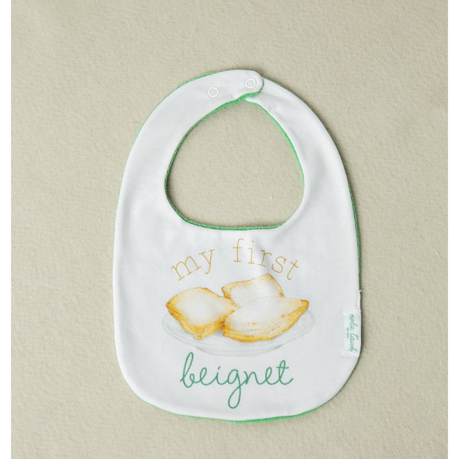 Baby bib with text and beignet illustration on a beige background