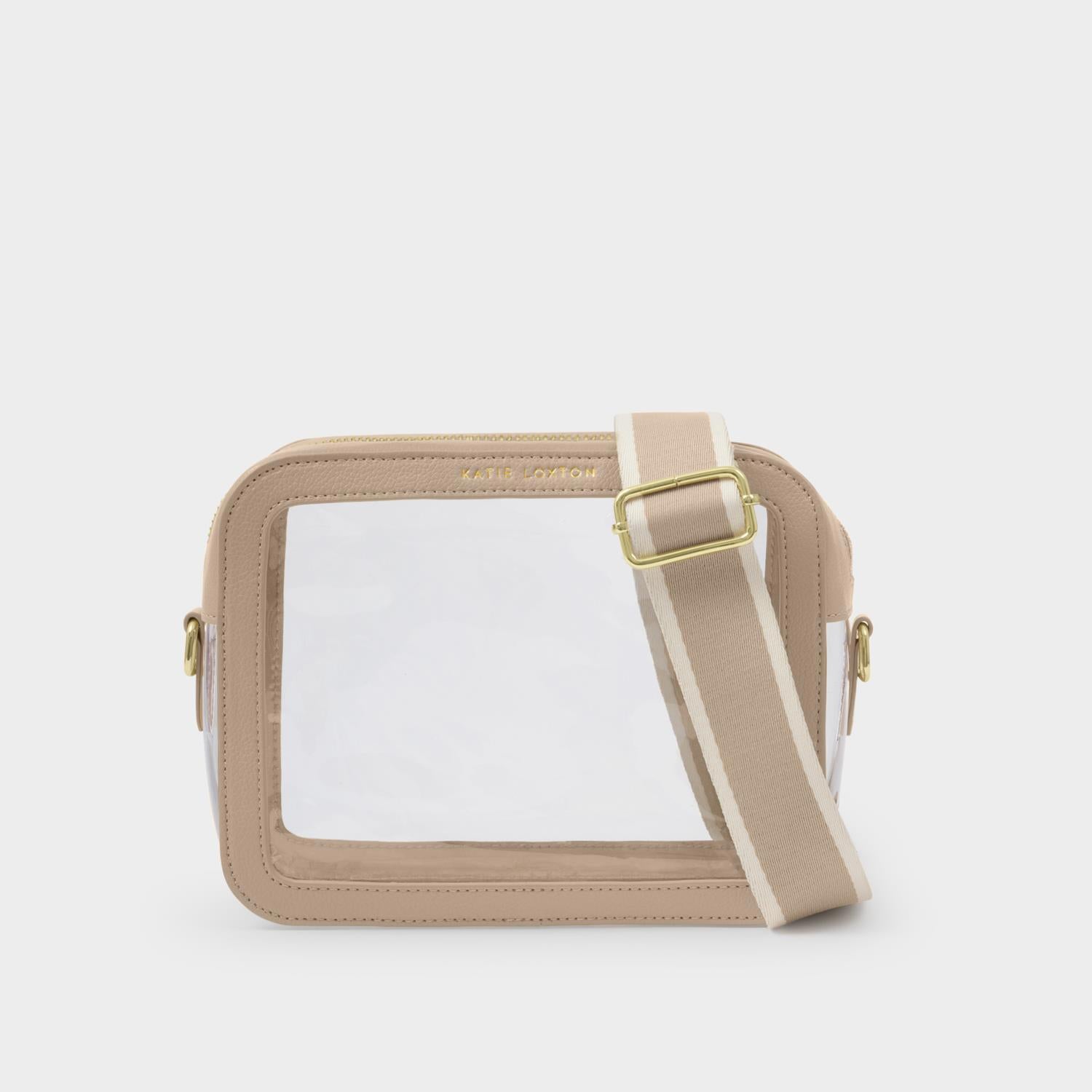 Product photography of a Katie Loxton beige and clear crossbody bag featuring a transparent PVC panel, gold logo hardware, and a wide striped adjustable shoulder strap on a neutral studio background