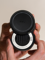 Commercial photograph for Pura of a matte black Smart Scent fragrance refill held in hands featuring a white Brooklyn Candle Studio label and vertical slotted vents