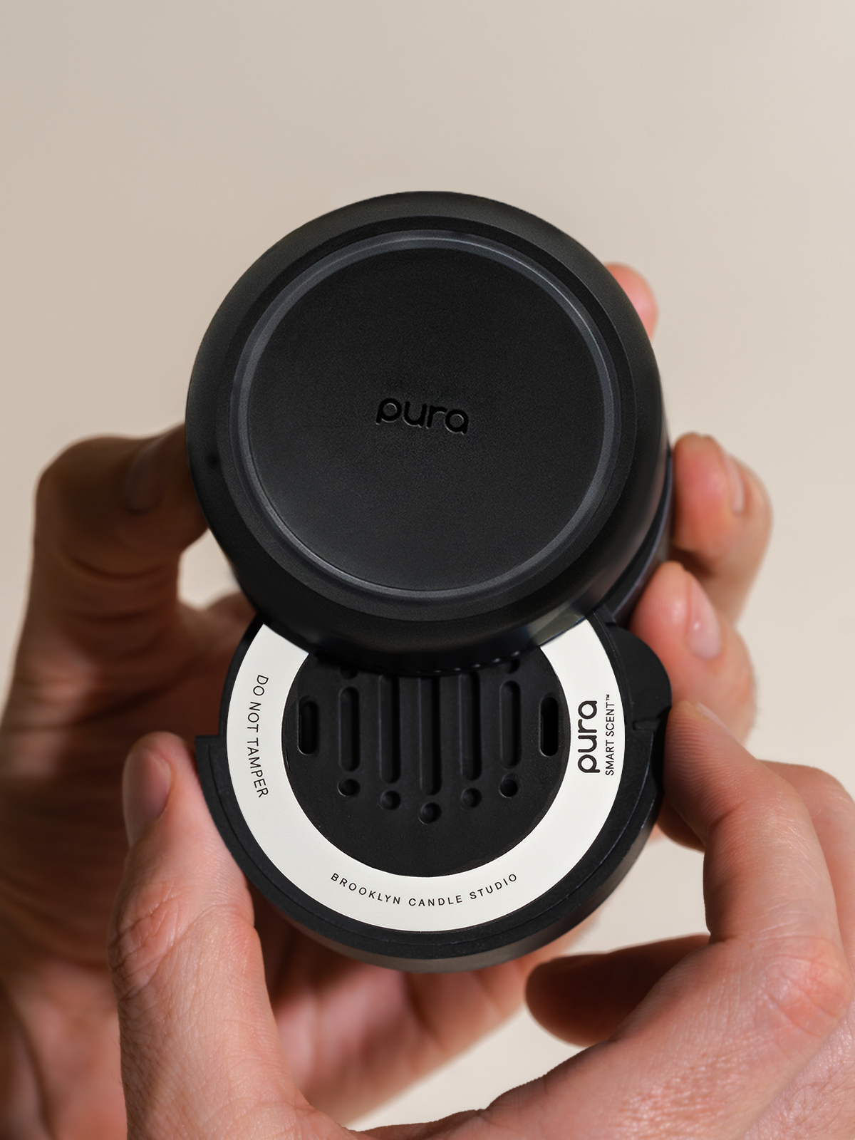 Commercial photograph for Pura of a matte black Smart Scent fragrance refill held in hands featuring a white Brooklyn Candle Studio label and vertical slotted vents