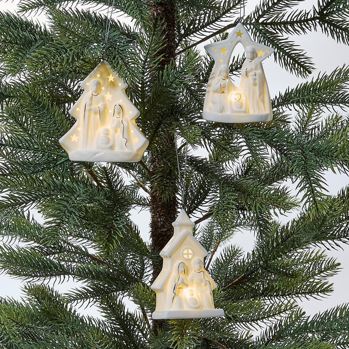 Glowing white porcelain nativity ornaments hanging on a Christmas tree