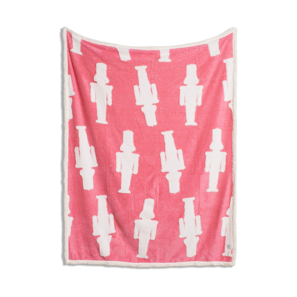 Pink throw blanket with white nutcracker pattern and white sherpa trim