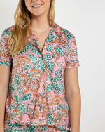 Woman wearing a pink short sleeve button down pajama top with a green and orange floral print