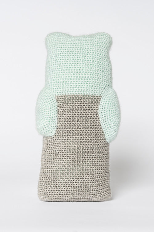 Crochet bear-shaped object with a mint green top and beige body featuring a distinct knit texture and small rounded arms on a plain white background