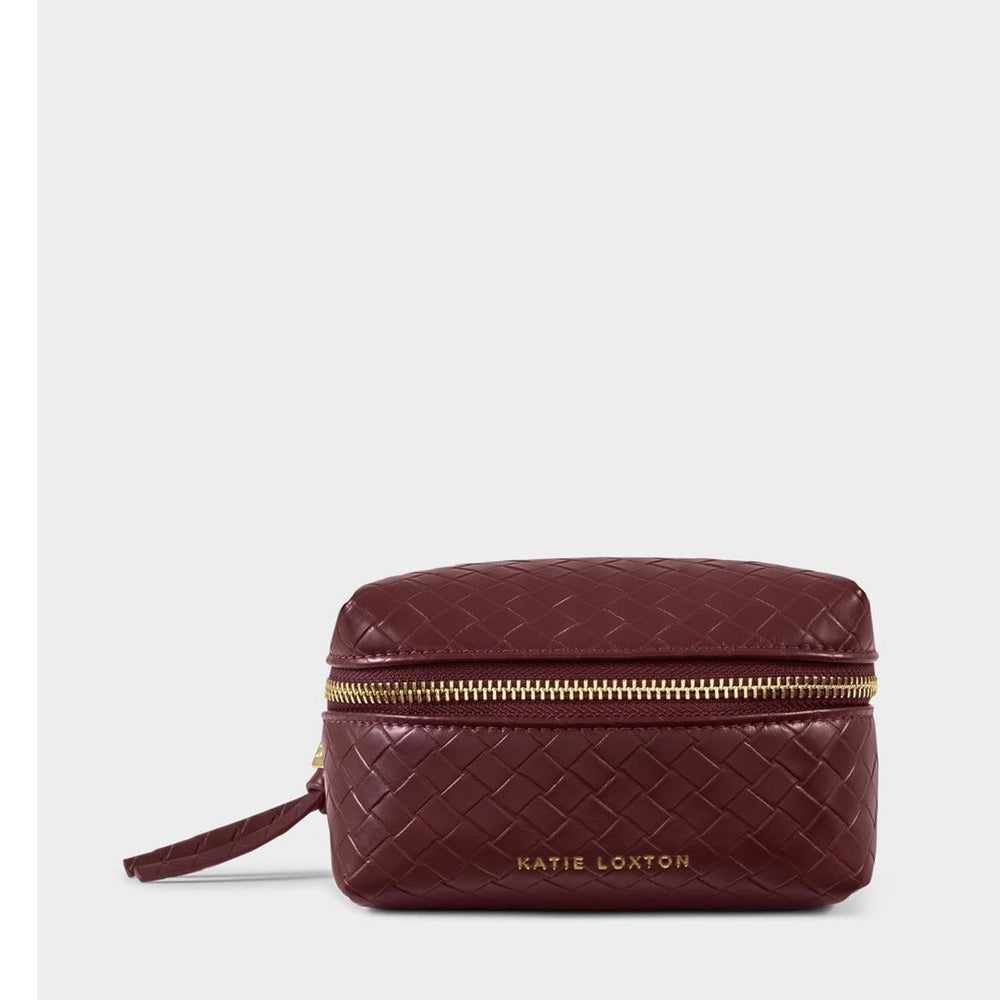Product photograph by Katie Loxton of a burgundy woven vegan leather wash bag on a neutral background featuring a gold-tone wrap-around zipper and debossed gold brand lettering