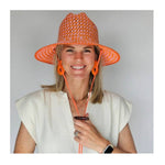 Woman wearing an orange woven hat with matching chin strap against a plain background