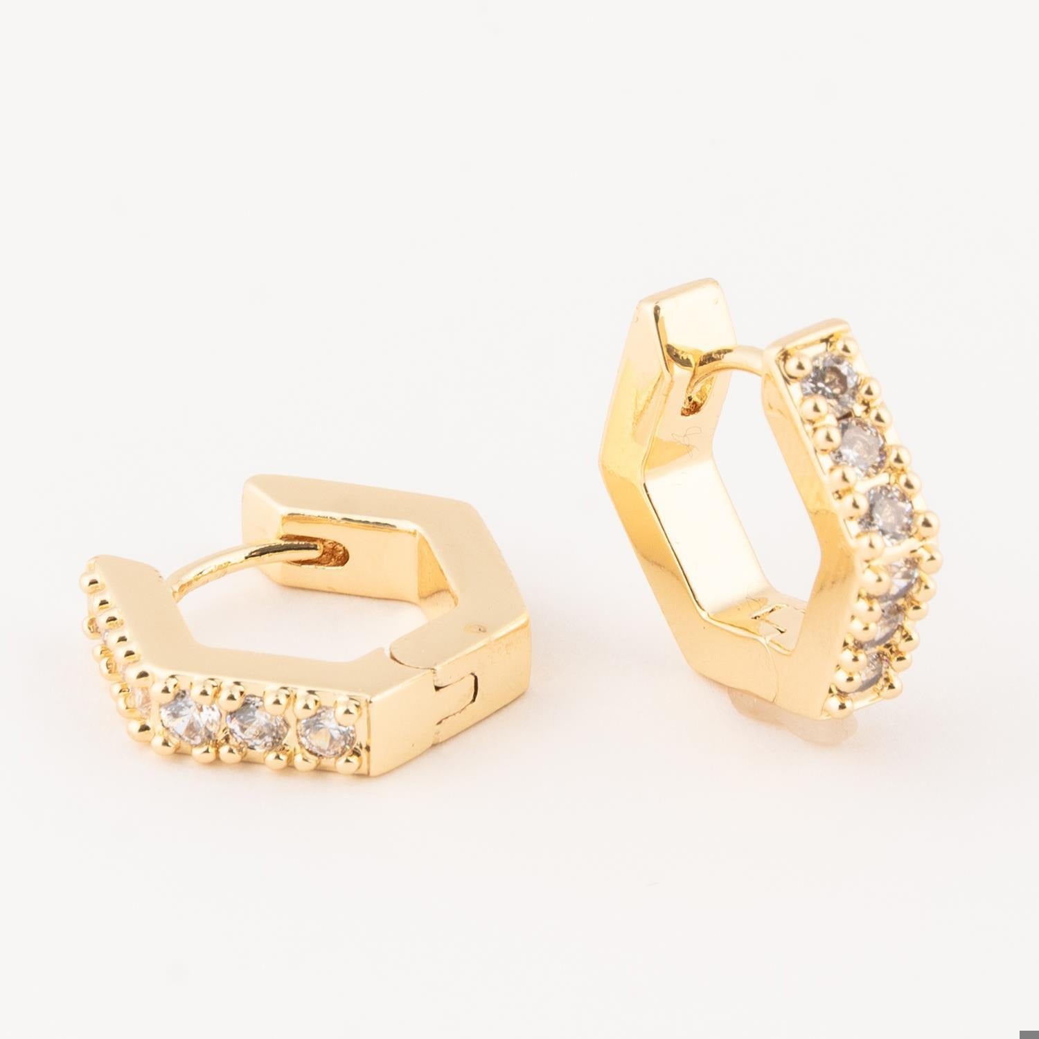 Gold-toned jewelry featuring a pair of geometric hexagonal huggie earrings with a row of sparkling clear round-cut stones and a polished finish displayed on a white studio background