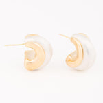 Jewelry pair of two-tone C-shaped hoop earrings featuring a matte white-silver finish entwined with polished gold sculptural curves against a minimalist white background