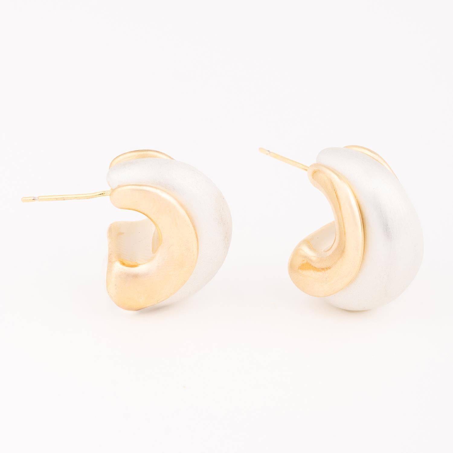 Jewelry pair of two-tone C-shaped hoop earrings featuring a matte white-silver finish entwined with polished gold sculptural curves against a minimalist white background