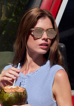 Woman wearing sunglasses and holding a coconut drink outdoors