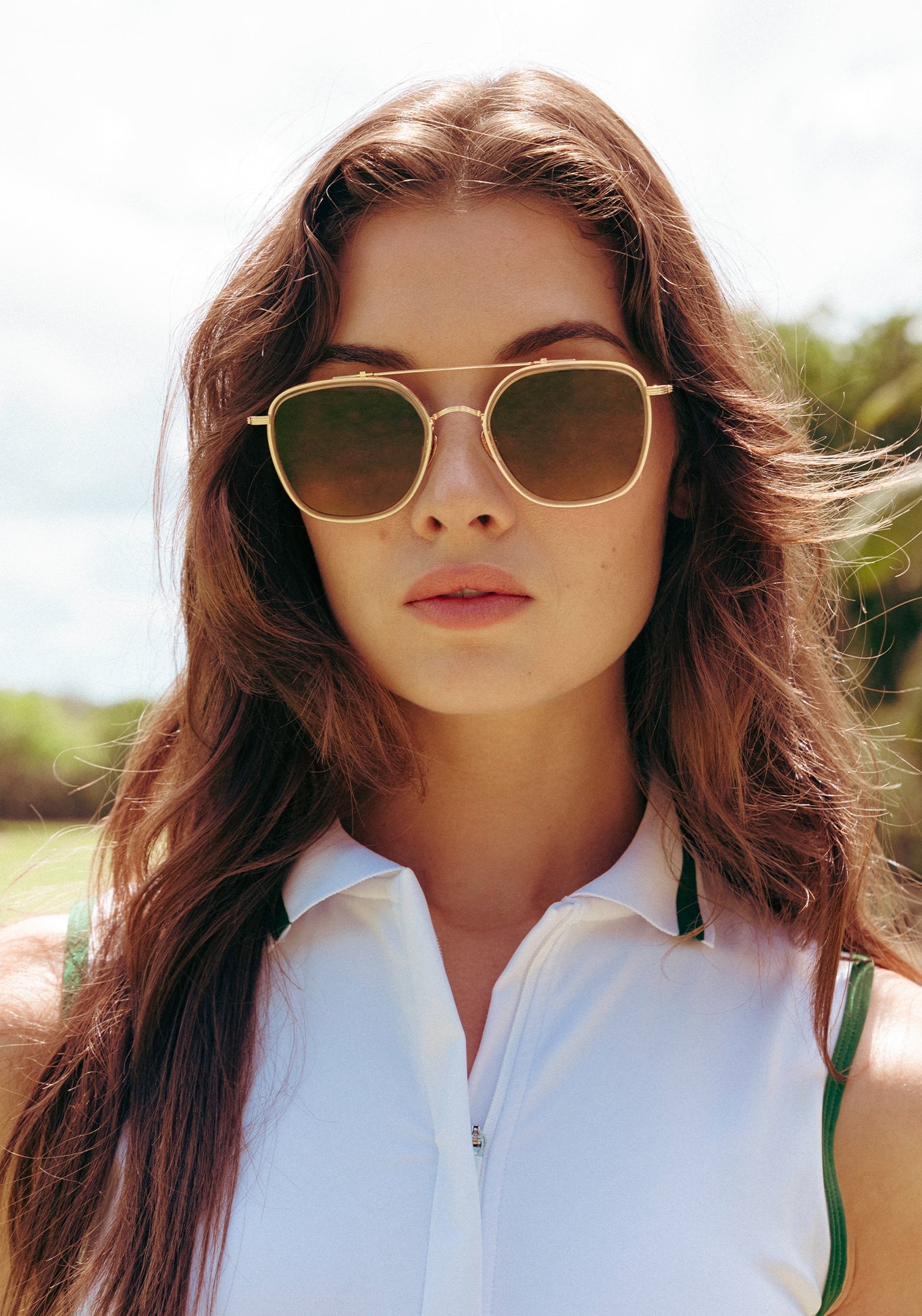 woman wearing gold aviator sunglasses with brown lenses standing in the outdoors