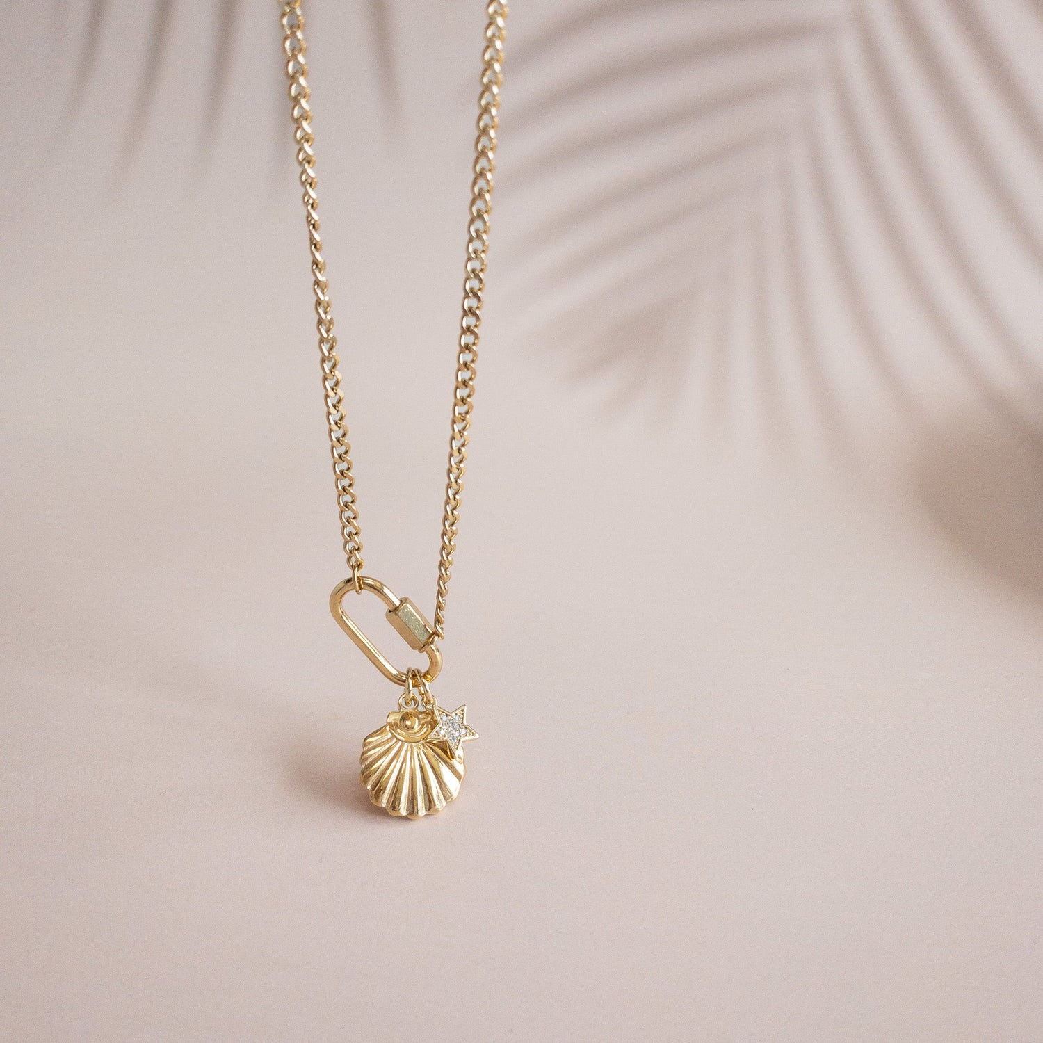 Gold chain necklace with a seashell and small star charm on a carabiner clasp