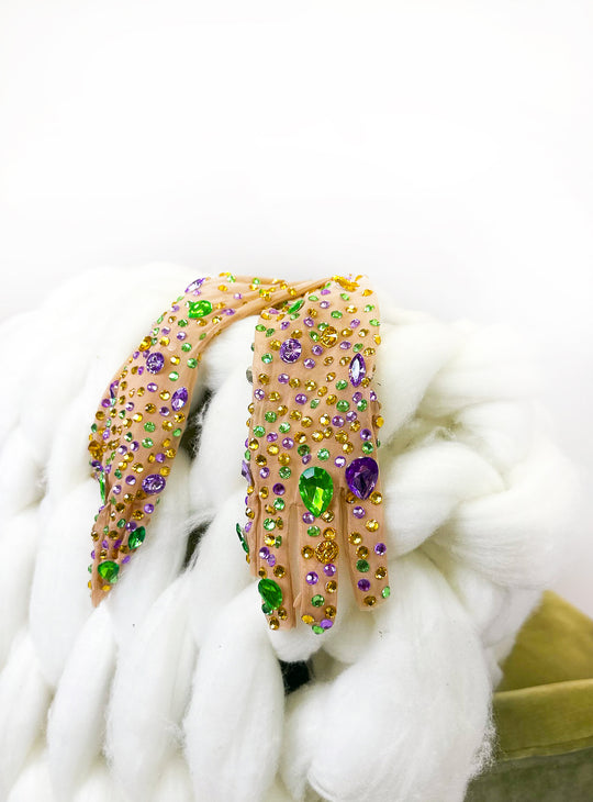 Sheer mesh gloves covered in purple, green and gold gems, resting on chunky white yarn