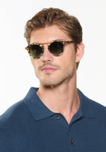 Man wearing round sunglasses with a blue shirt on a white background