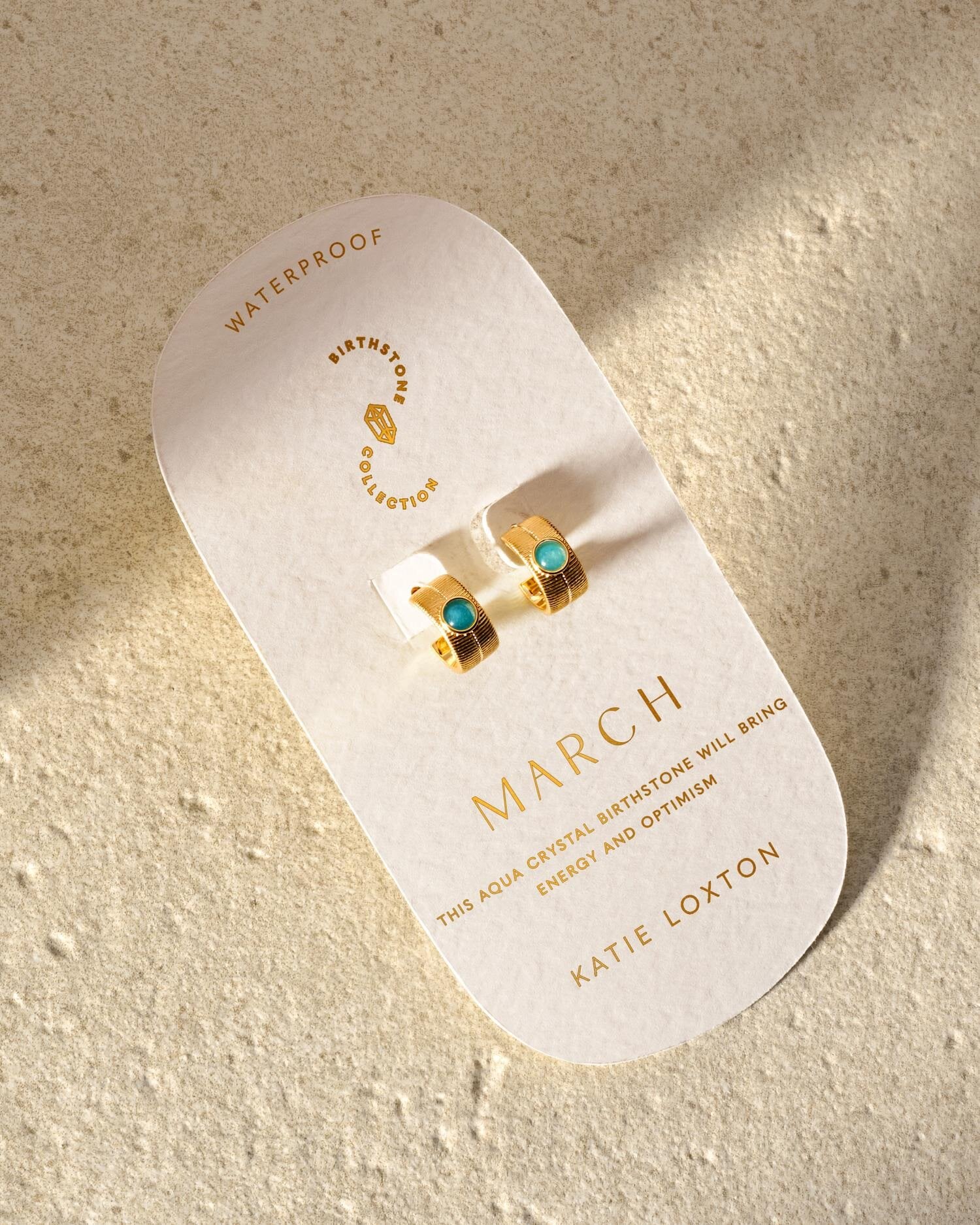Gold hoop earrings with aqua stones on a March birthstone display card